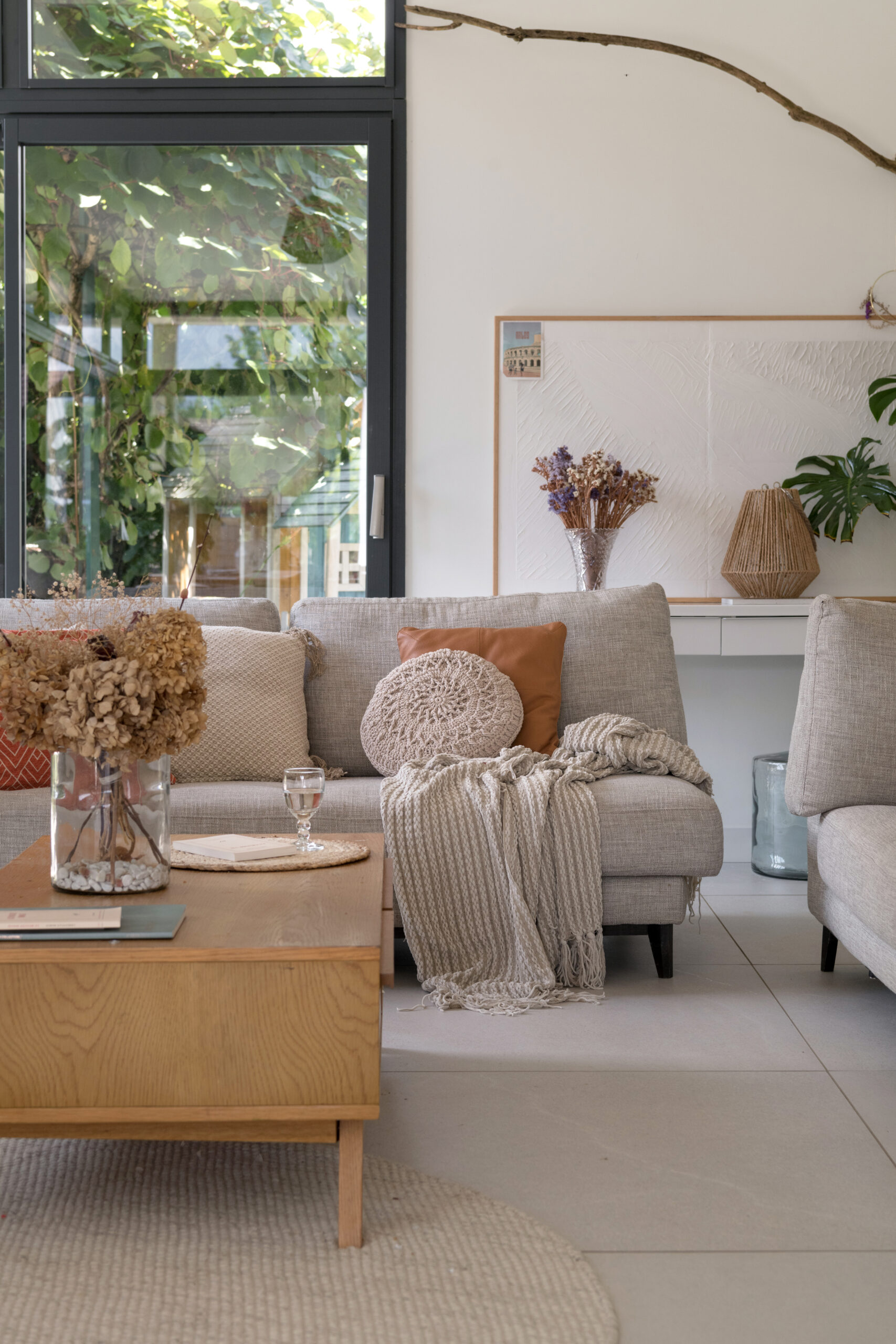 Salon avec canapé beige, tapis en laine tressée et ouverture sur l’extérieur