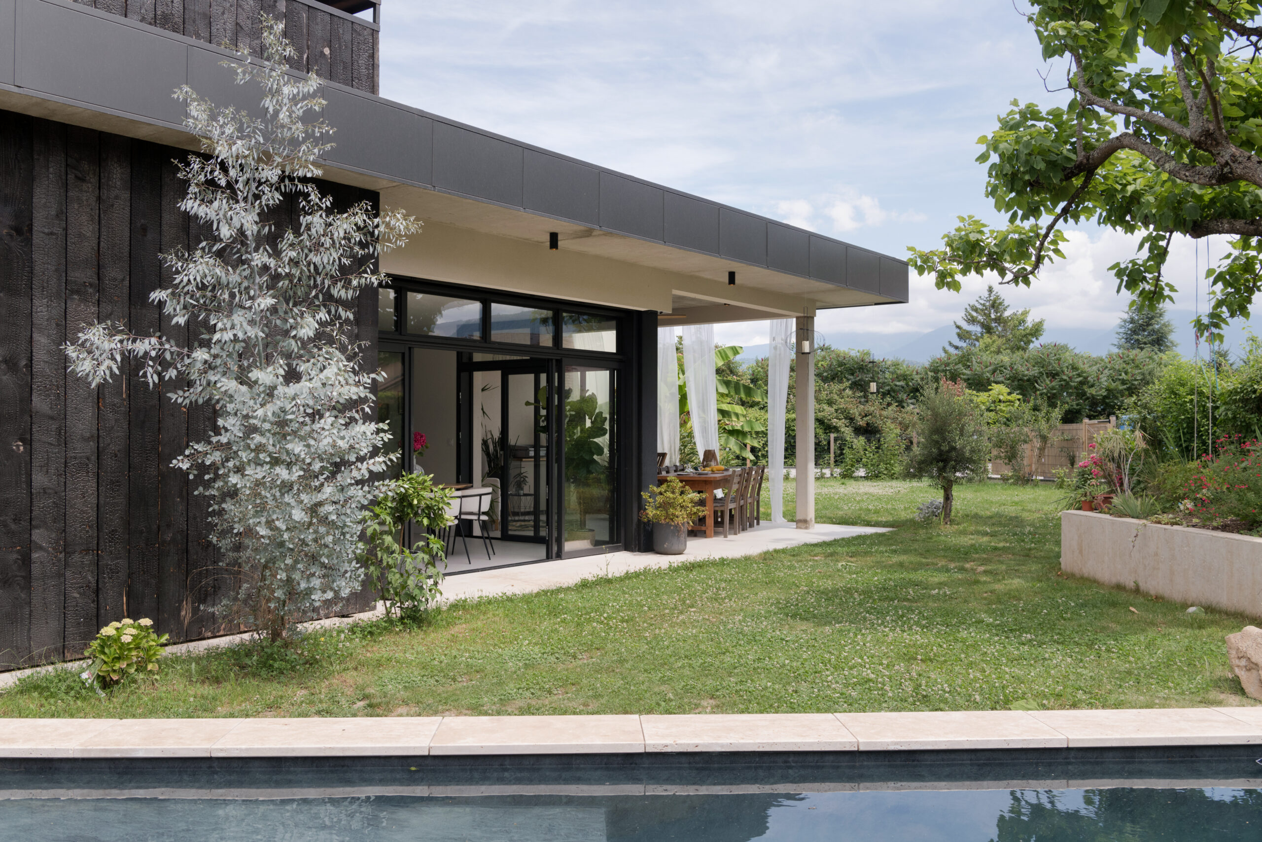 Maison contemporaine avec bardage en bois brûlé, jardin arboré, terrasse et piscine bassin.